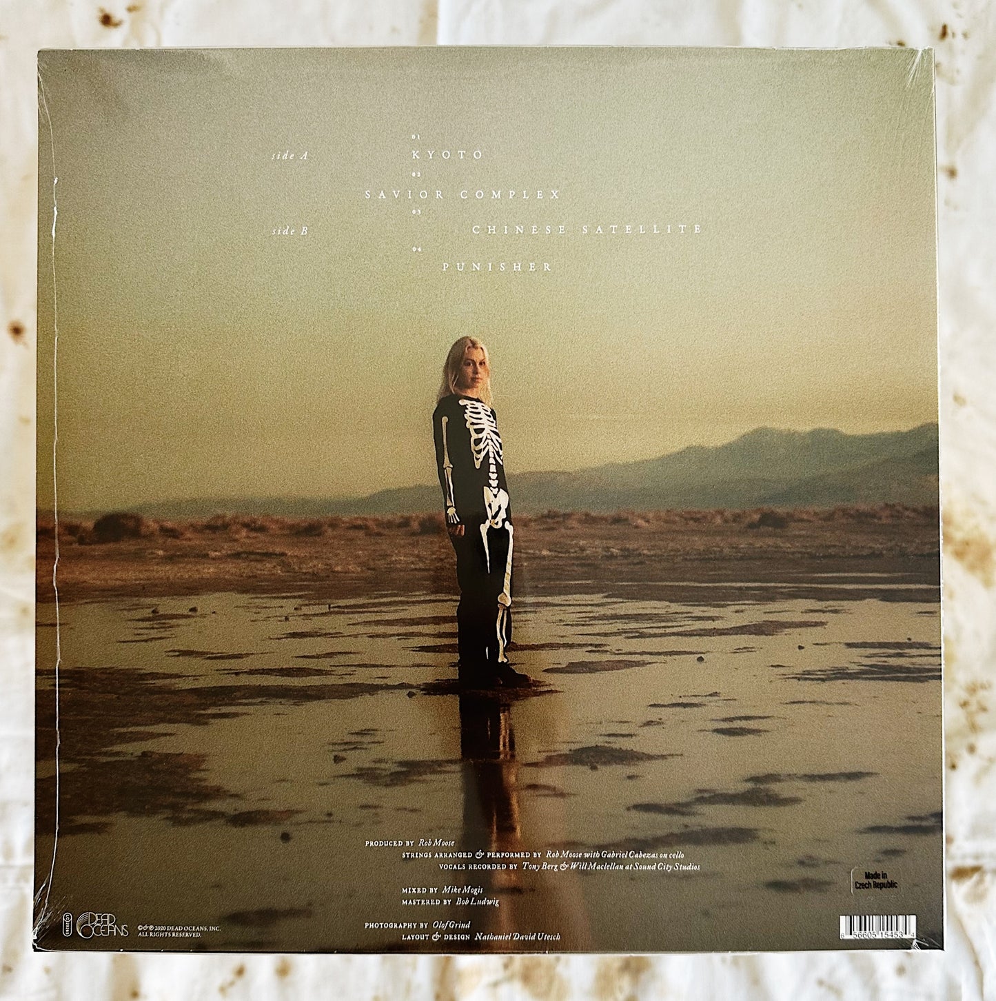This is the back cover of Phoebe Bridgers & Rob Moose LP record vinyl Copycat Killer. Phoebe is standing on the cover in a skeleton outfit standing straight looking into the camera. She is standing in a muddy area in the middle of a desert