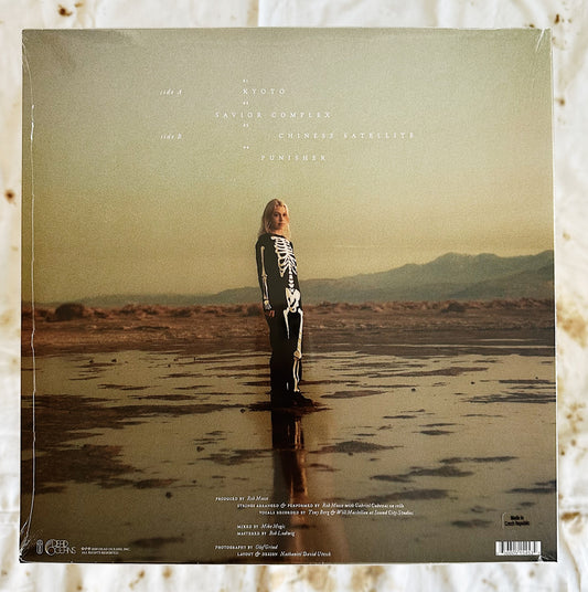 This is the back cover of Phoebe Bridgers & Rob Moose LP record vinyl Copycat Killer. Phoebe is standing on the cover in a skeleton outfit standing straight looking into the camera. She is standing in a muddy area in the middle of a desert