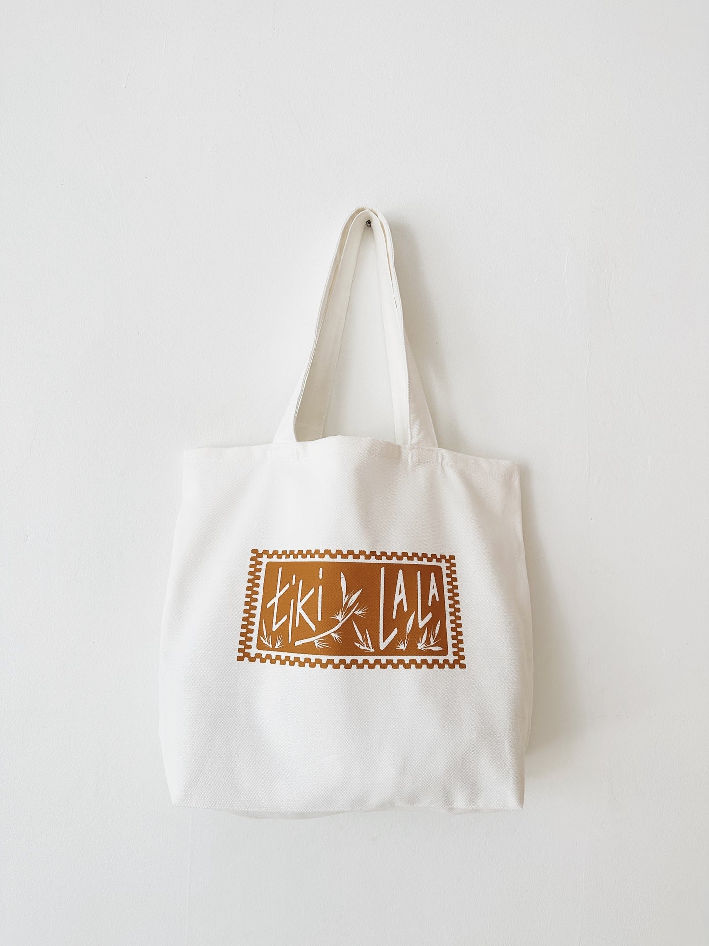This Tiki La La Stamp Tote is a soft cream cotton tote with a tan stamp logo with bamboo print