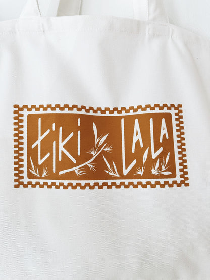 This Tiki La La Stamp Tote is a soft cream cotton tote with a tan stamp logo with bamboo print